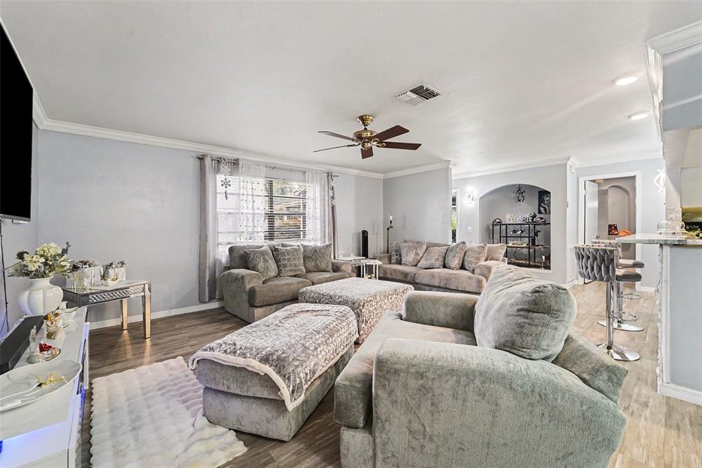 A living room features gray sofas, a patterned ottoman, wood-look flooring, and a ceiling fan — 13020 SUGAR CREEK BOULEVARD, HUDSON, FL