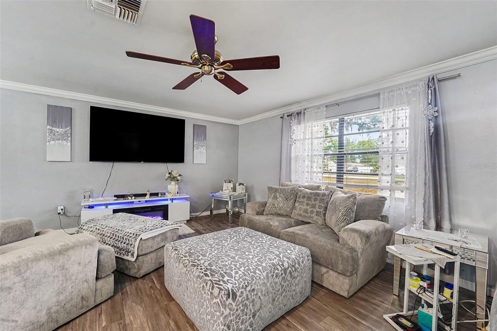 A living room features gray walls, wood-look flooring, a ceiling fan, and gray upholstered furniture — 13020 SUGAR CREEK BOULEVARD, HUDSON, FL