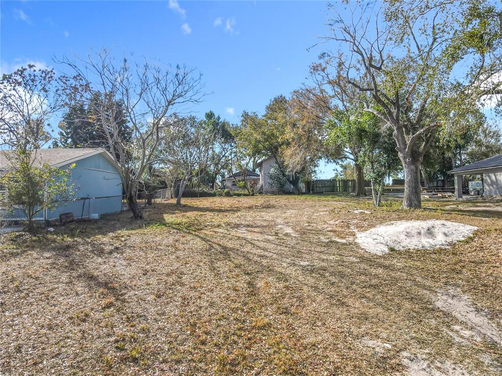 A large, grassy backyard features several mature trees, a blue shed, and a sand pile — 309 WEAVER AVENUE, LAKE WALES, FL