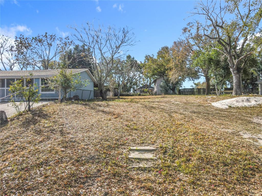 A grassy yard slopes upward toward a light blue house and several mature trees — 309 WEAVER AVENUE, LAKE WALES, FL