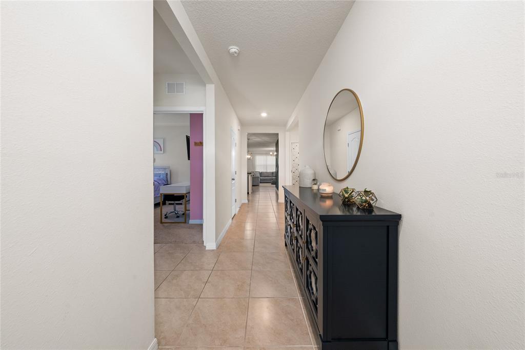 A tiled hallway features a black console table, a round mirror, and an adjacent bedroom — 687 GRIFFON AVENUE, LAKE ALFRED, FL