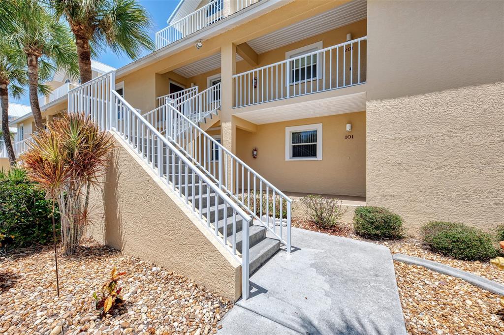 An exterior view of a two-story tan building with a concrete staircase and white railings — 6610 GASPARILLA PINES BOULEVARD UNIT 202, ENGLEWOOD, FL