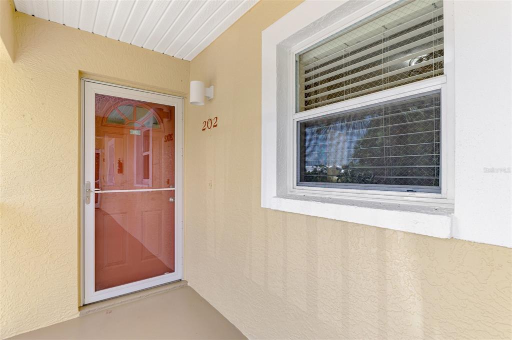 The exterior entrance of a residential unit features a storm door and a single window — 6610 GASPARILLA PINES BOULEVARD UNIT 202, ENGLEWOOD, FL