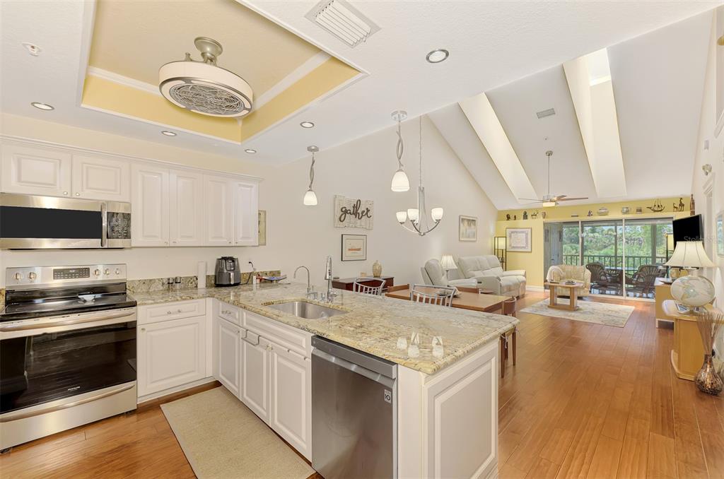 An open-concept kitchen with white cabinets and granite countertops overlooks a living area with vaulted ceilings — 6610 GASPARILLA PINES BOULEVARD UNIT 202, ENGLEWOOD, FL