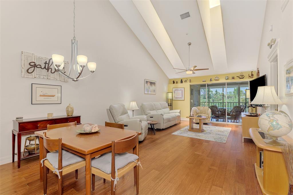A living and dining area features vaulted ceilings, wood flooring, and a sliding glass door — 6610 GASPARILLA PINES BOULEVARD UNIT 202, ENGLEWOOD, FL