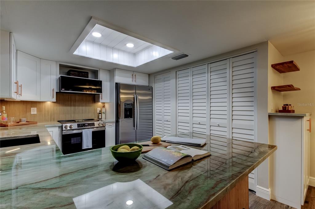 A kitchen sink area features a copper faucet, marble-look countertop, and natural wood shelving — 2673 SABAL SPRINGS CIRCLE UNIT 201, CLEARWATER, FL