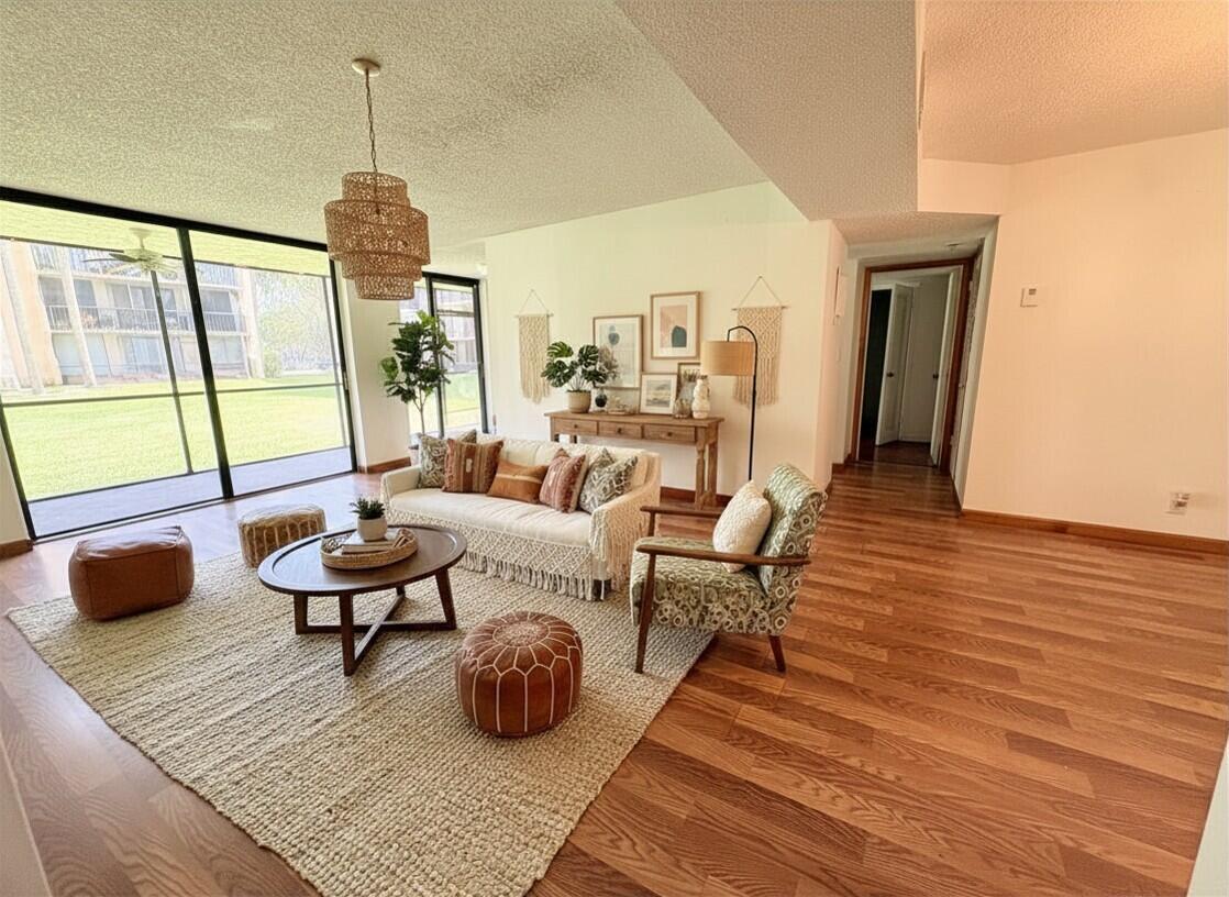 A living room features wood flooring, a textured area rug, a sofa, and a glass door — 3590 Blue Lake Drive # 104, Pompano Beach FL 33064, POMPANO BEACH, FL