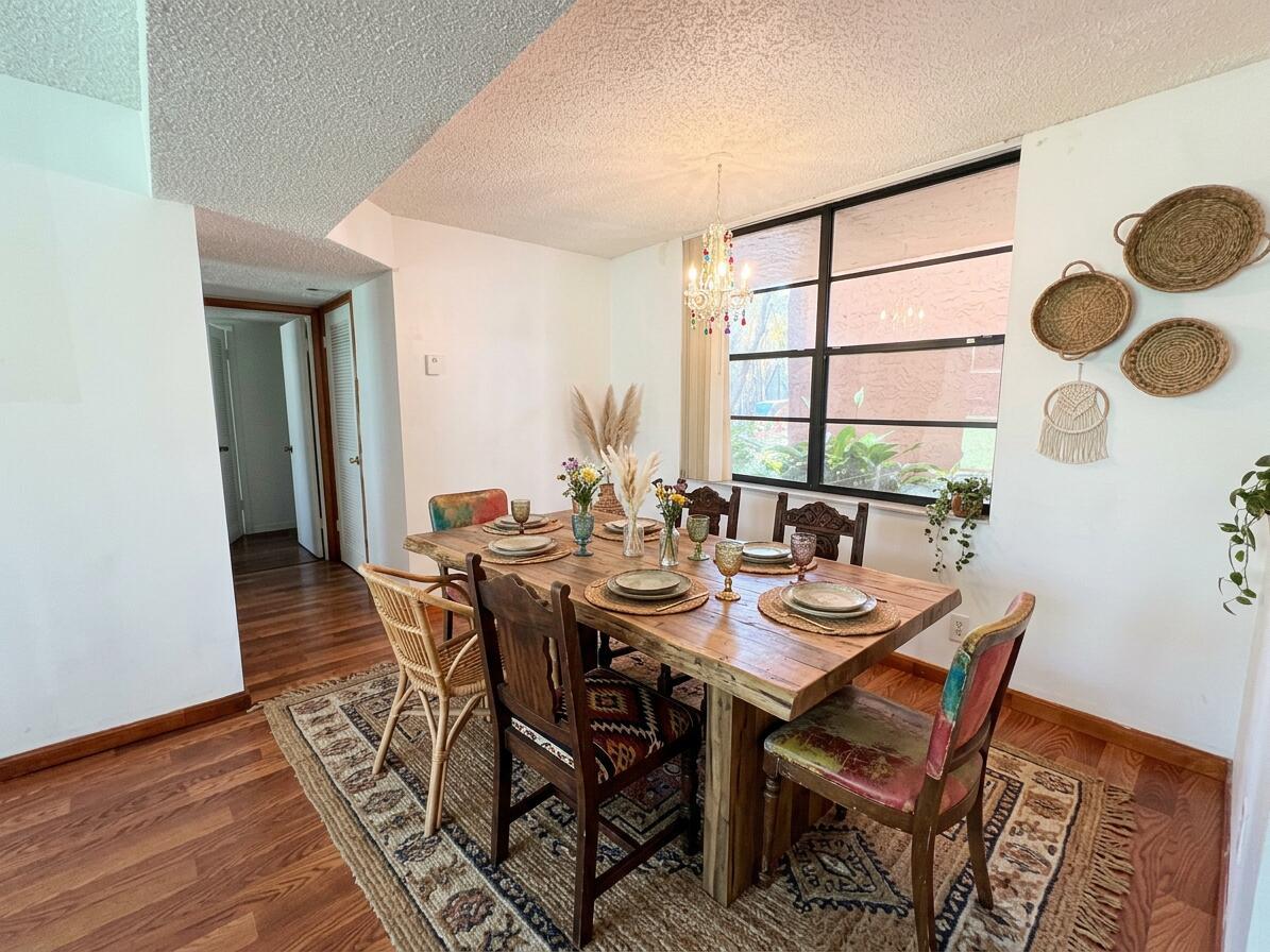 A dining room features a rustic wooden table, eclectic chairs, and a large window — 3590 Blue Lake Drive # 104, Pompano Beach FL 33064, POMPANO BEACH, FL