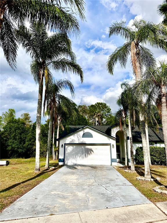 A white house with a two-car garage sits behind a concrete driveway and palm trees — 1757 QUAIL RIDGE LOOP, KISSIMMEE, FL