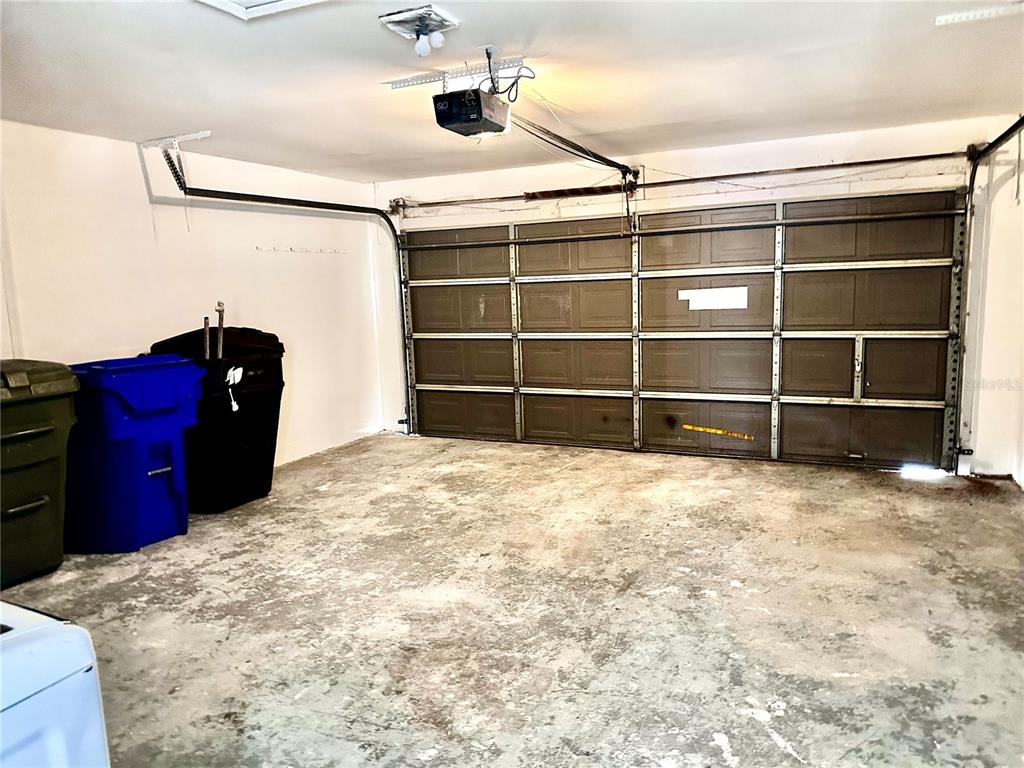 A garage with a concrete floor, a sectional metal door, and three large trash bins — 1757 QUAIL RIDGE LOOP, KISSIMMEE, FL