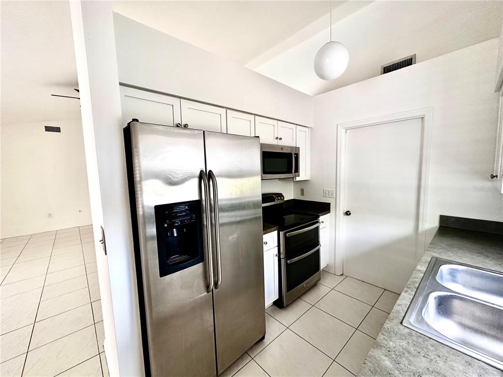A kitchen features stainless steel appliances, white cabinets, and light-colored tile flooring — 1757 QUAIL RIDGE LOOP, KISSIMMEE, FL