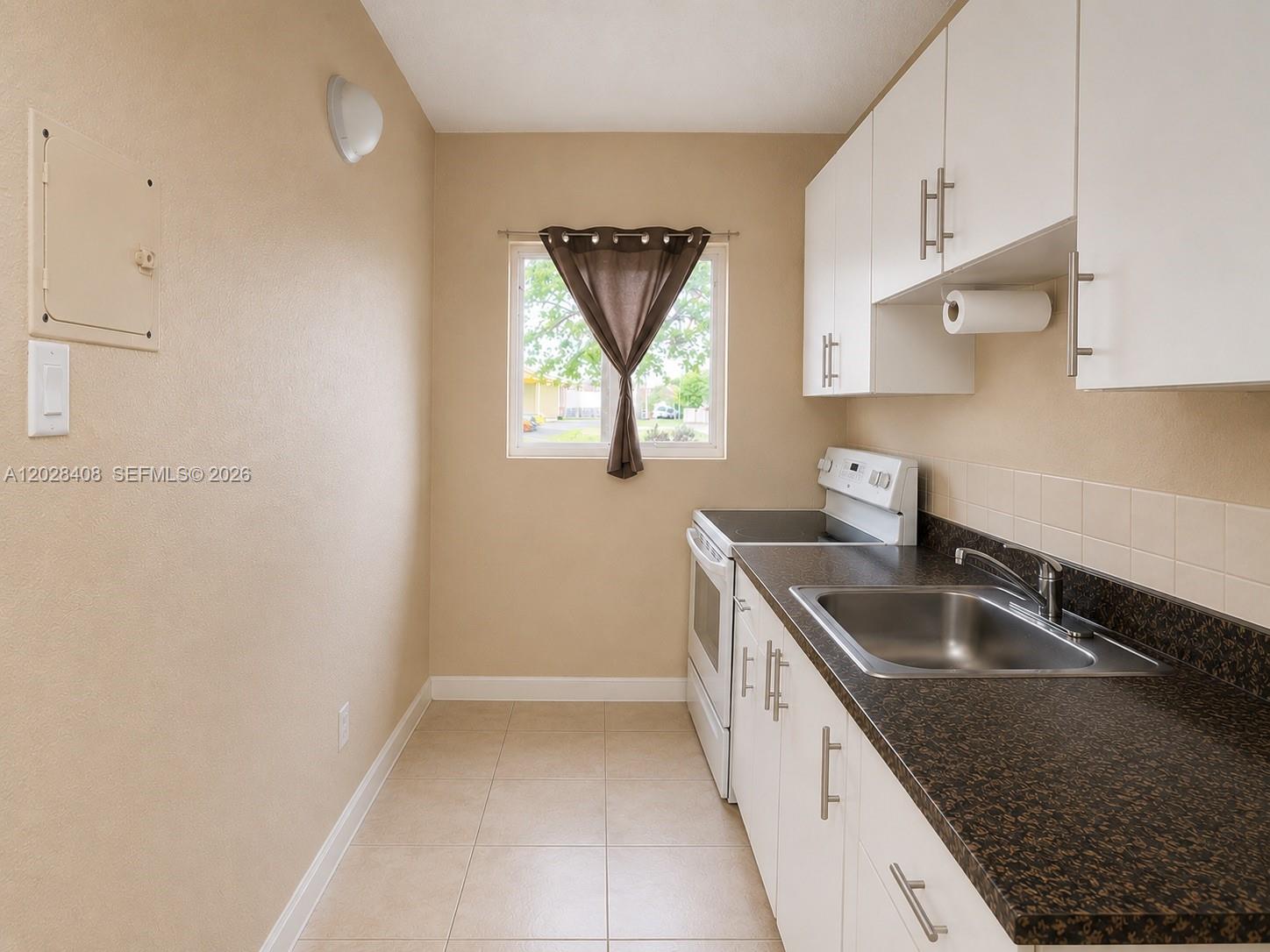 A galley kitchen features white cabinets, dark countertops, a stainless steel sink, and tile flooring — 520 SW 6th Ave # 2, Homestead FL 33030, HOMESTEAD, FL