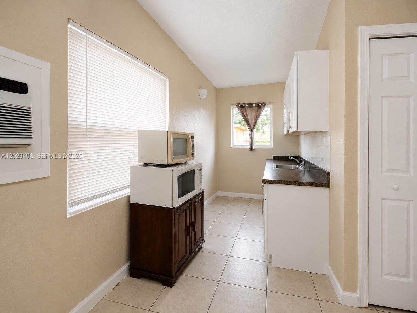 A small kitchen features white cabinets, a sink, tile flooring, and two stacked microwaves — 520 SW 6th Ave # 2, Homestead FL 33030, HOMESTEAD, FL