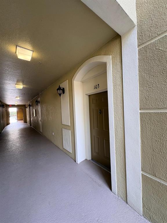 An outdoor apartment hallway features tan stucco walls, recessed lighting, and a brown door numbered 103 — 3344 ROBERT TRENT JONES DRIVE UNIT 10305, ORLANDO, FL