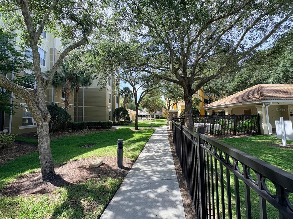 A paved walkway leads between a multi-story apartment building and a fenced community pool area — 3344 ROBERT TRENT JONES DRIVE UNIT 10305, ORLANDO, FL