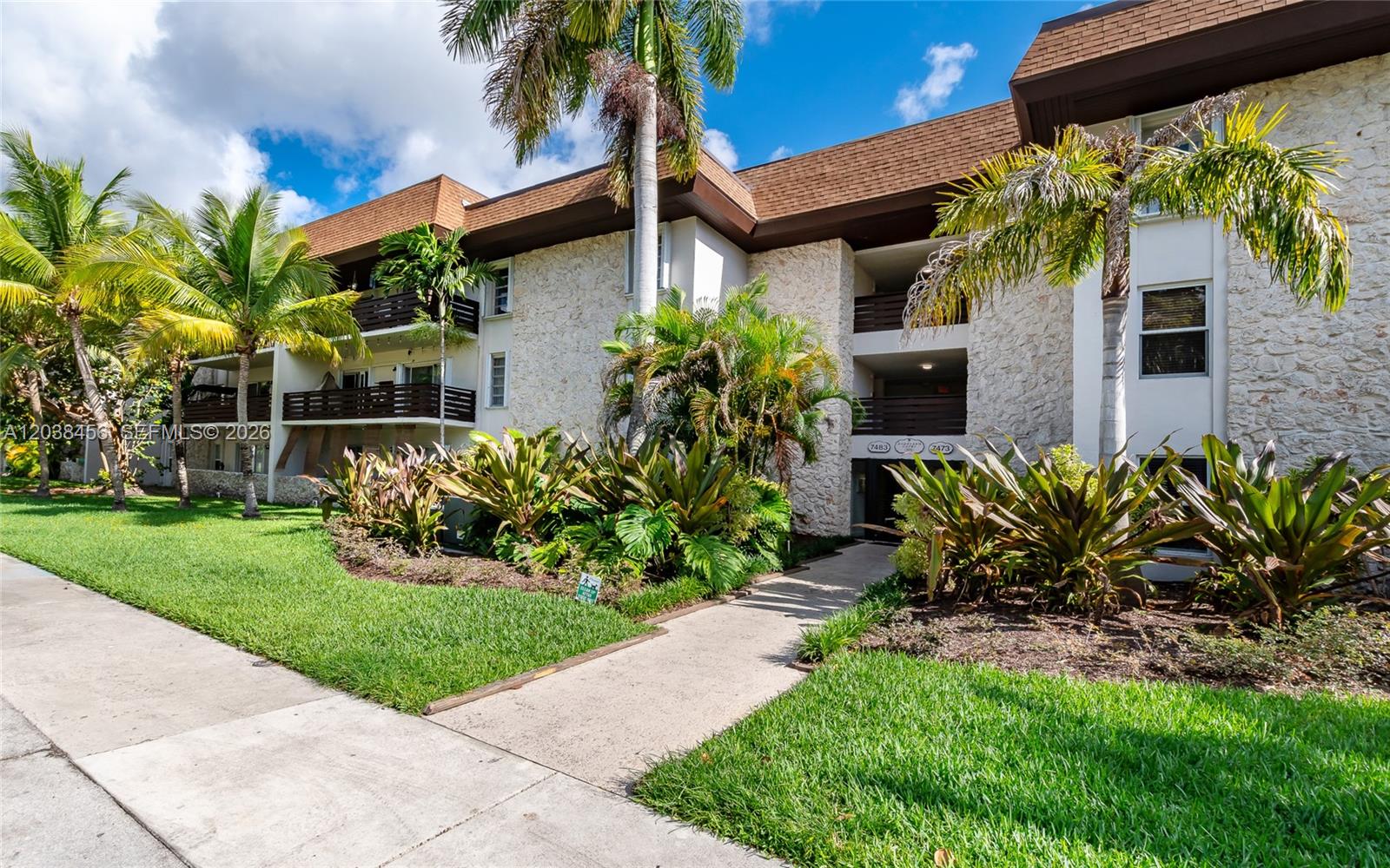 A multi-story apartment building features stone siding, brown trim, and lush tropical landscaping — 7483 SW 82nd St # A206, Miami FL 33143, MIAMI, FL