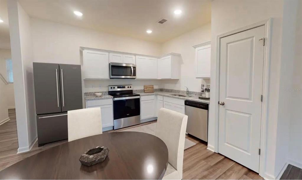 A kitchen features white cabinets, stainless steel appliances, granite countertops, and a dining table — 6195 DAERR RIDGE ST STREET, ZEPHYRHILLS, FL