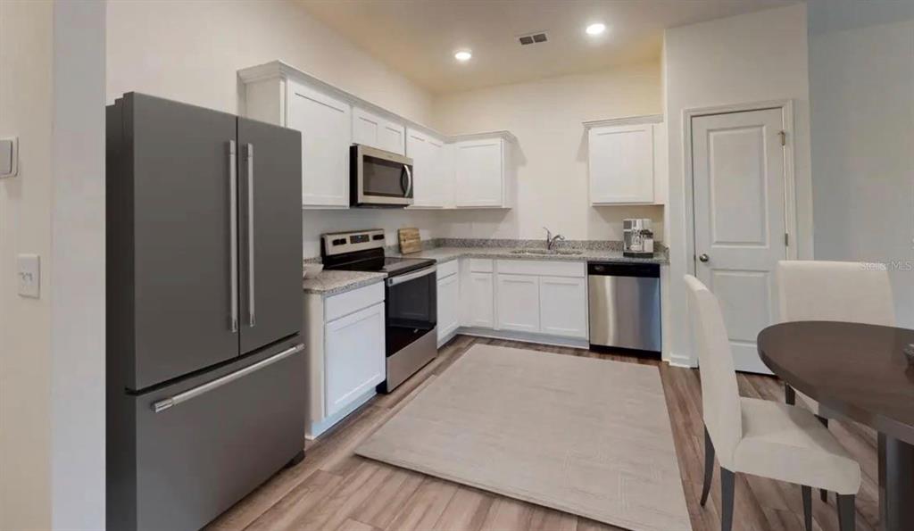 A kitchen features white cabinets, stainless steel appliances, granite countertops, and light wood-look flooring — 6195 DAERR RIDGE ST STREET, ZEPHYRHILLS, FL