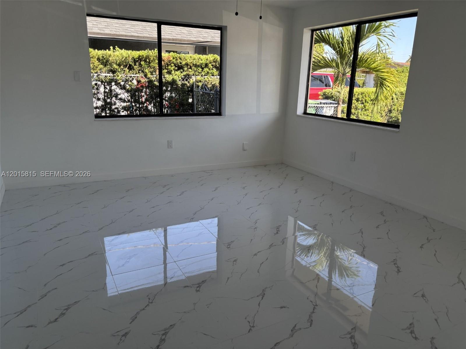 An empty room features white marble-look tile flooring and two windows overlooking a yard — 7343 SW 21st St # 0, Miami FL 33155, MIAMI, FL