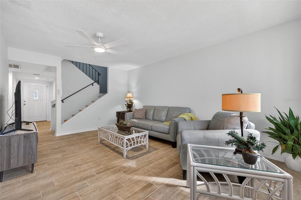 A living room features light wood-look tile flooring, a gray sofa, and a staircase — 6490 CAPE HATTERAS WAY NE UNIT 2, ST PETERSBURG, FL