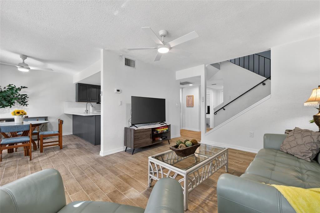 A living room with wood-look tile floors, a glass coffee table, and an adjacent kitchen — 6490 CAPE HATTERAS WAY NE UNIT 2, ST PETERSBURG, FL
