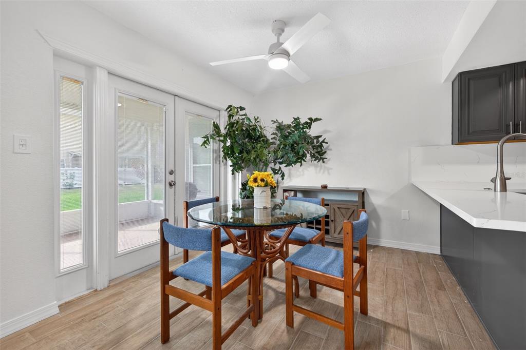 A dining area features a glass-topped table, blue chairs, a ceiling fan, and sliding doors — 6490 CAPE HATTERAS WAY NE UNIT 2, ST PETERSBURG, FL