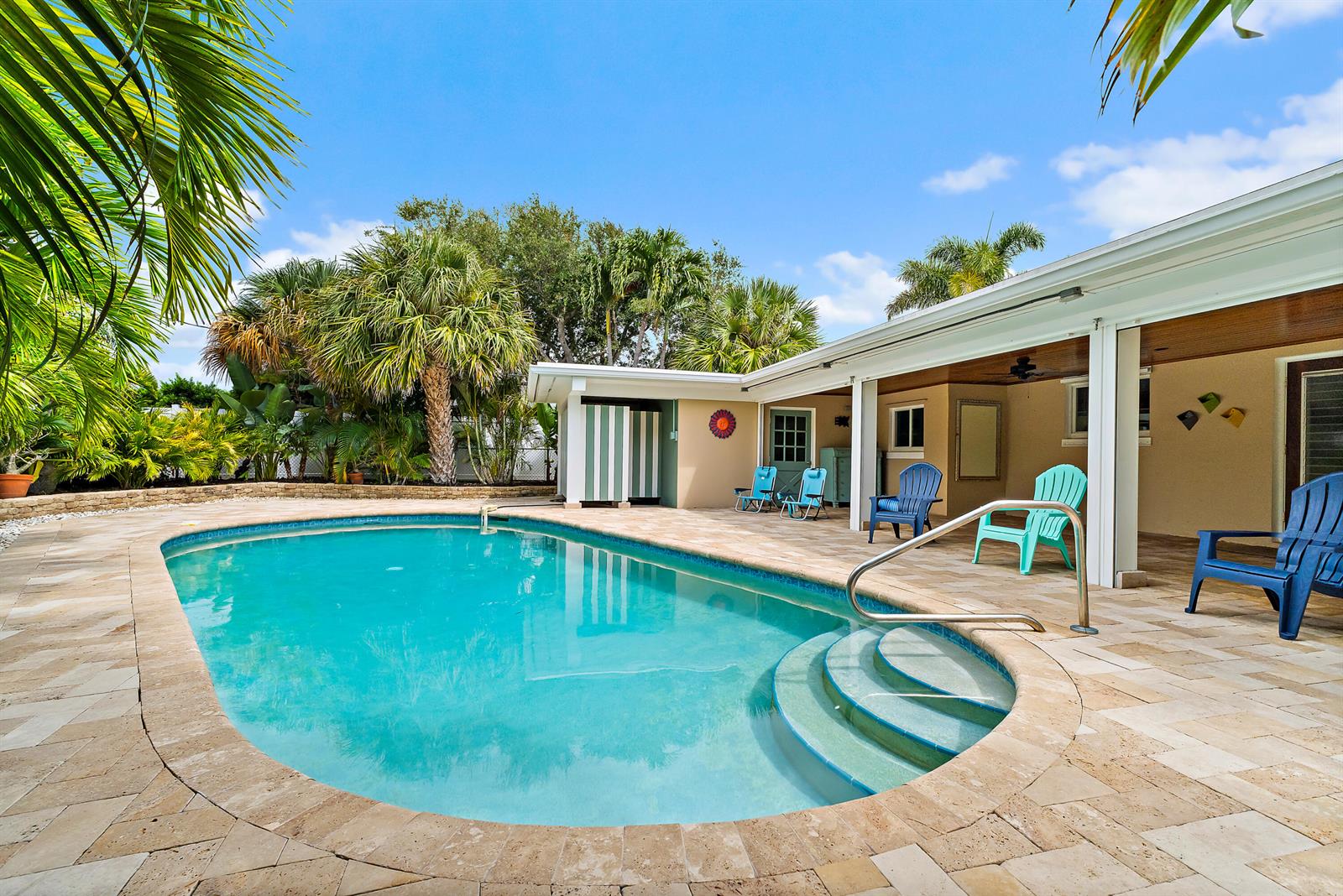 A swimming pool with stone decking and patio chairs sits beside a house with palm trees — 440 Jupiter Lane, Juno Beach FL 33408, JUNO BEACH, FL