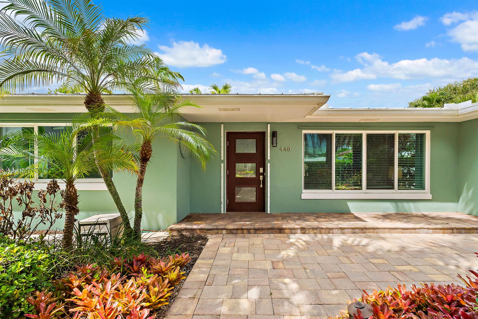 The exterior of a light green house features a brown front door and a paved walkway — 440 Jupiter Lane, Juno Beach FL 33408, JUNO BEACH, FL