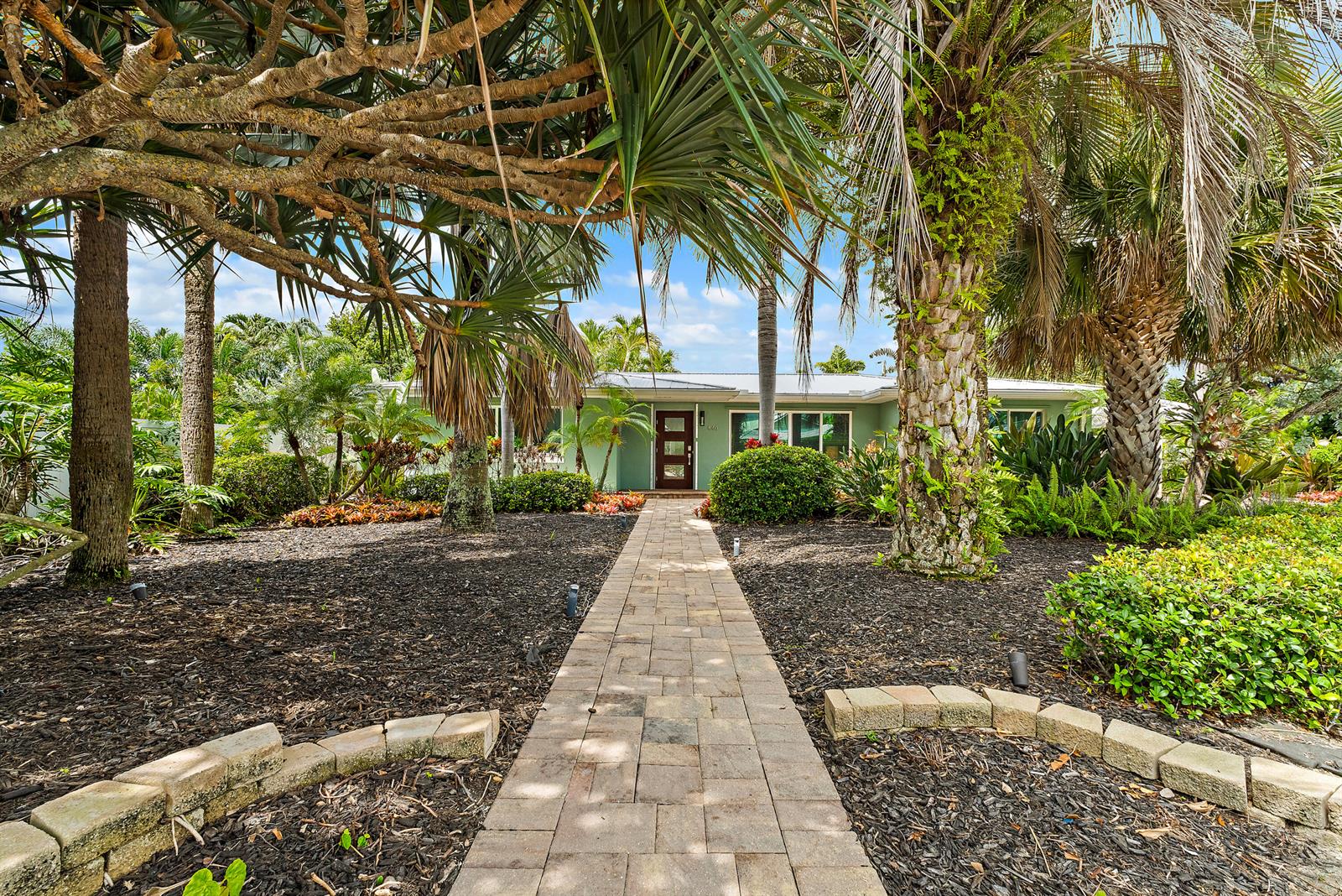 A stone walkway leads to the front entrance of a green house surrounded by palm trees — 440 Jupiter Lane, Juno Beach FL 33408, JUNO BEACH, FL