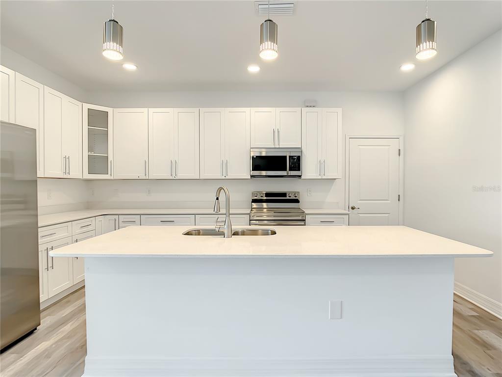 A modern kitchen features white cabinets, a large island with a sink, and stainless appliances — 5123 WEATHERTON STREET, NORTH PORT, FL