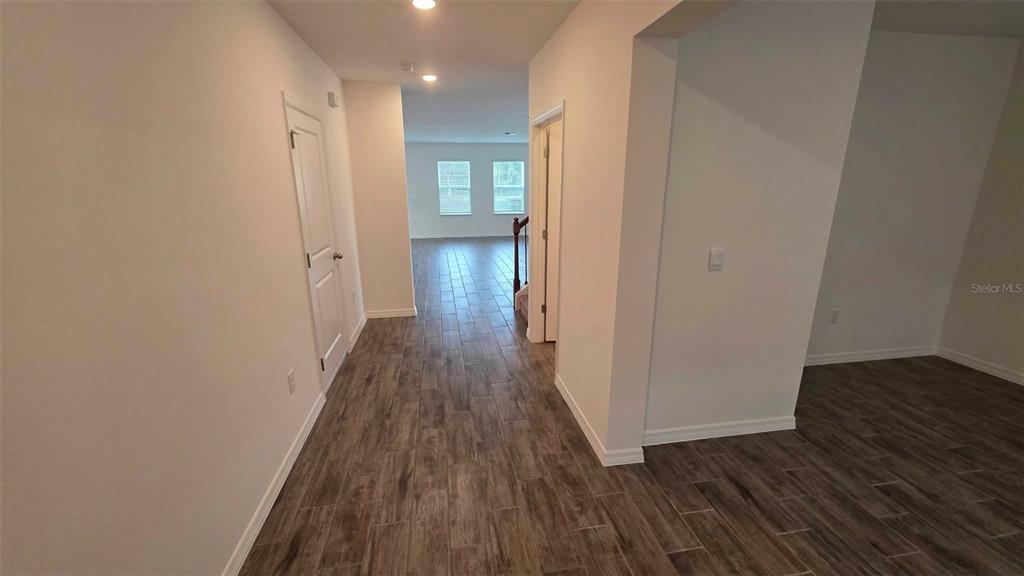 A hallway with wood-look tile flooring leads toward a bright living area with windows — 3262 VICEROY COURT, POINCIANA, FL