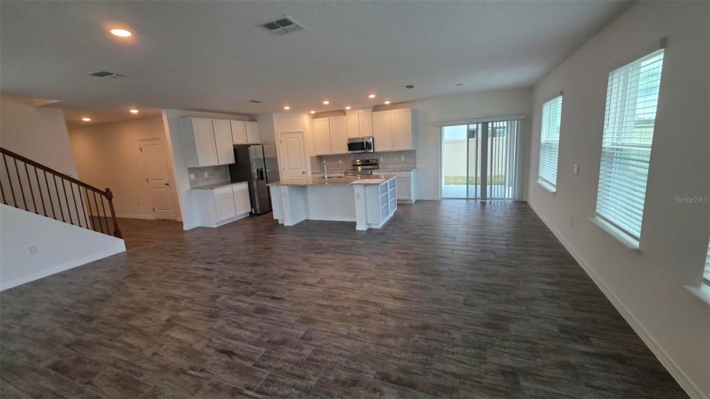 An open-concept kitchen and living area feature white cabinets, a center island, and wood-look flooring — 3262 VICEROY COURT, POINCIANA, FL
