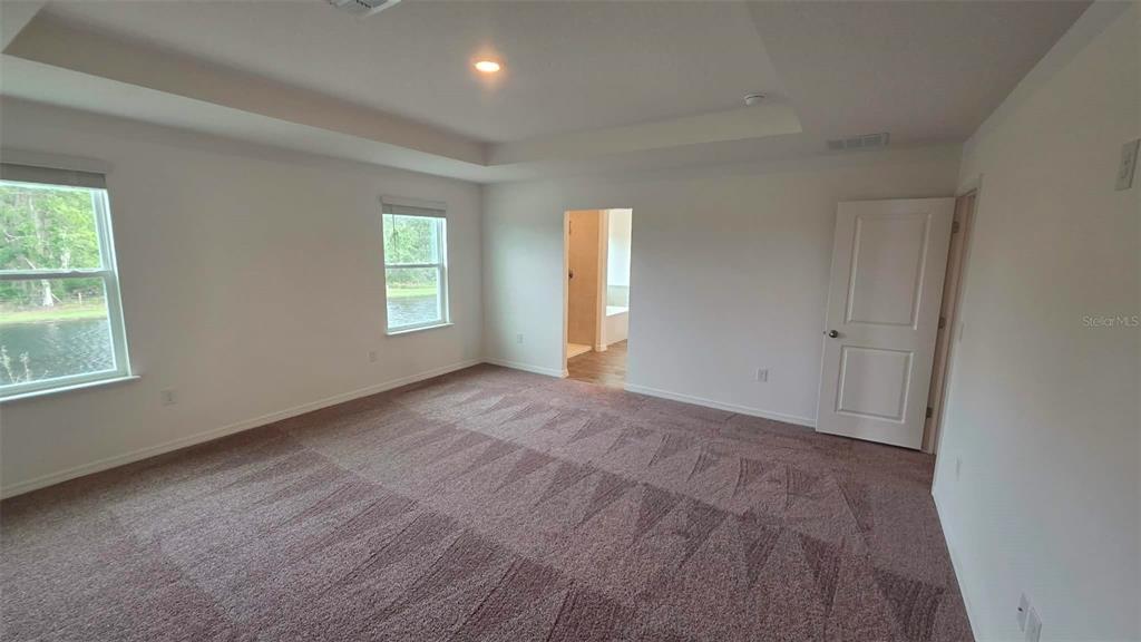 A carpeted bedroom features a tray ceiling, two windows, and a doorway leading to a bathroom — 3262 VICEROY COURT, POINCIANA, FL