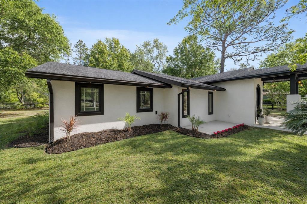 A white stucco house exterior with dark trim, a shingled roof, and landscaped garden beds — 5721 SW 31ST STREET, OCALA, FL