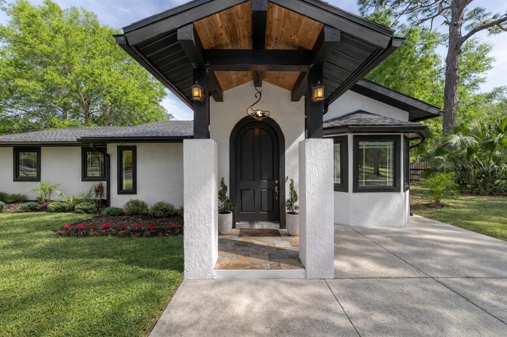 A white stucco house features a black arched front door under a wood-paneled porch roof — 5721 SW 31ST STREET, OCALA, FL