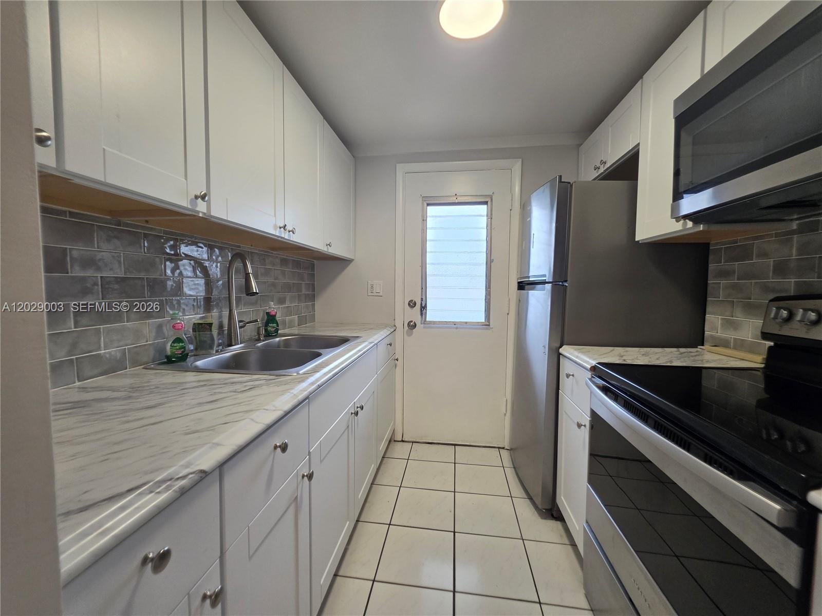 A galley kitchen features white cabinets, marble-look countertops, gray subway tile, and stainless steel appliances — 17000 NE 14th Ave # 109, Miami FL 33162, MIAMI, FL