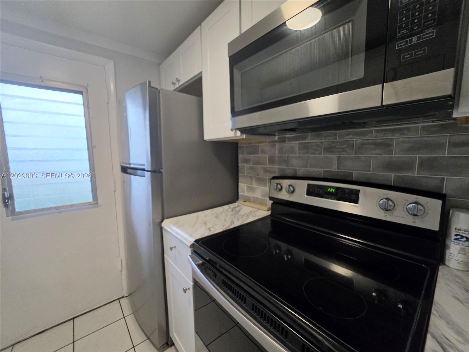 A kitchen features stainless steel appliances, white cabinets, marble-look countertops, and a gray subway tile backsplash — 17000 NE 14th Ave # 109, Miami FL 33162, MIAMI, FL