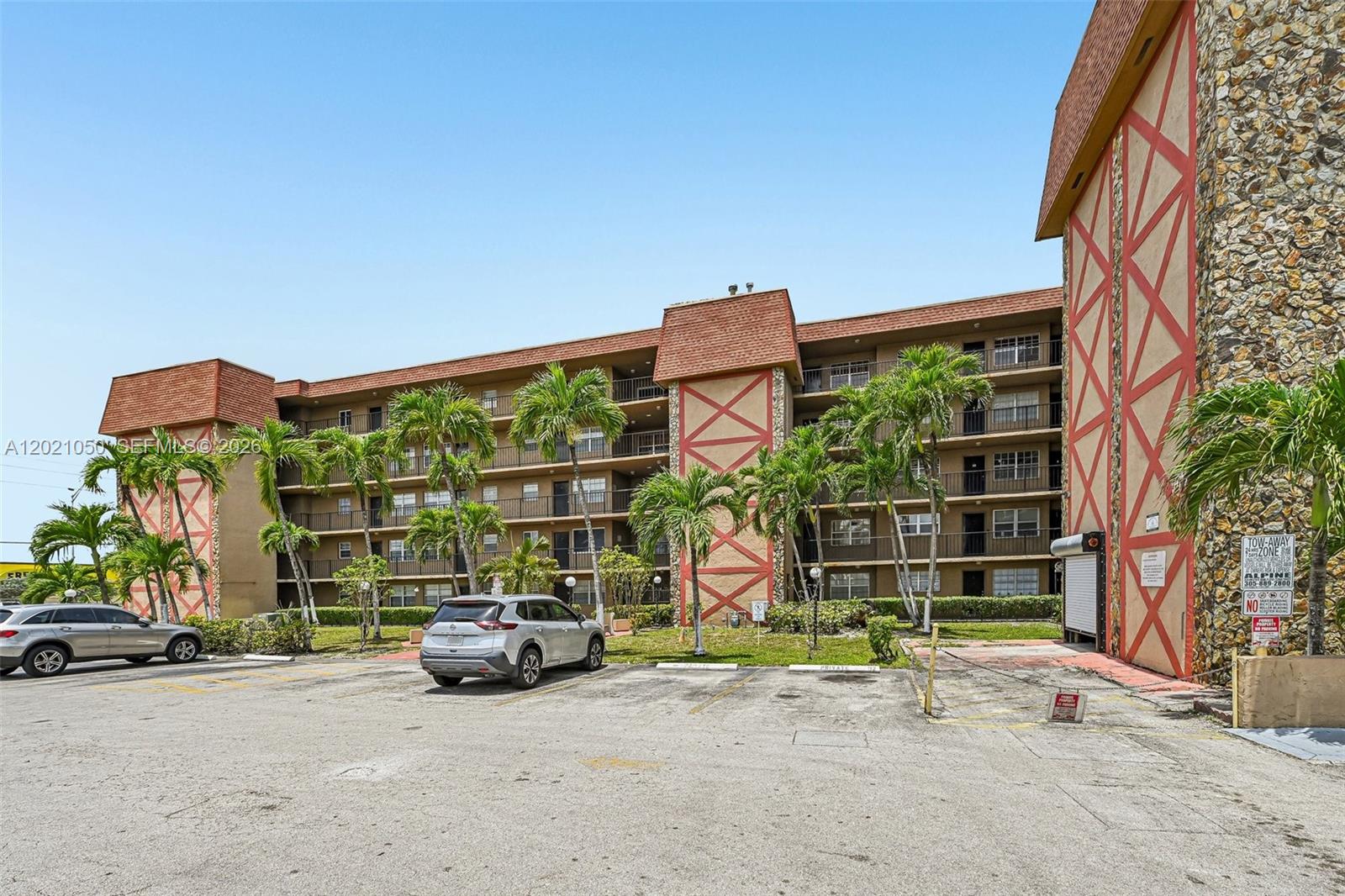 A multi-story apartment building with a brown facade and stone accents sits behind a parking lot — 6575 W 4th Ave # 507, Hialeah FL 33012, HIALEAH, FL