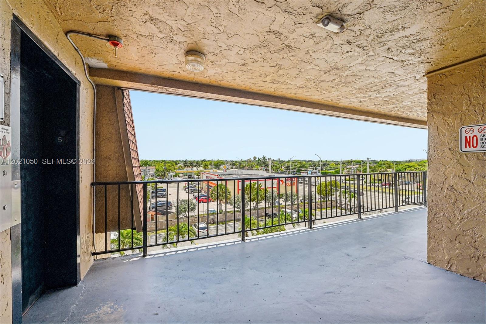 A covered balcony with a black metal railing overlooks a parking lot and street — 6575 W 4th Ave # 507, Hialeah FL 33012, HIALEAH, FL