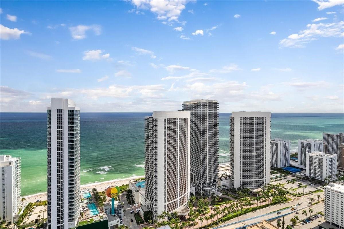 An aerial view shows several tall residential towers along a sandy beach and ocean — 4010 S Ocean Drive # R1102, Hollywood FL 33019, HOLLYWOOD, FL