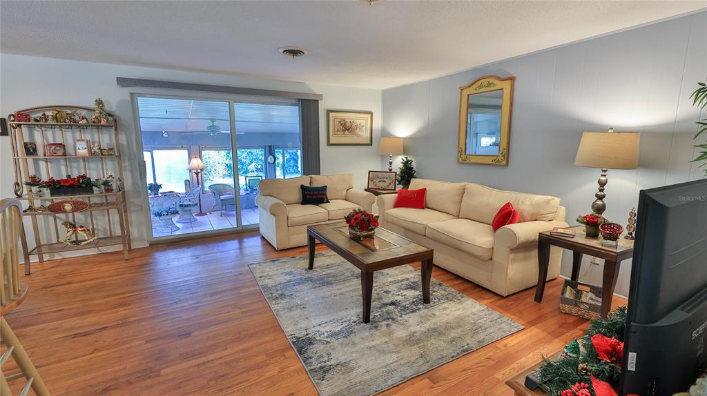 A living room features light-colored sofas, a coffee table, wood-look flooring, and a sliding glass door — 515 OLIVER DRIVE, NEW SMYRNA BEACH, FL