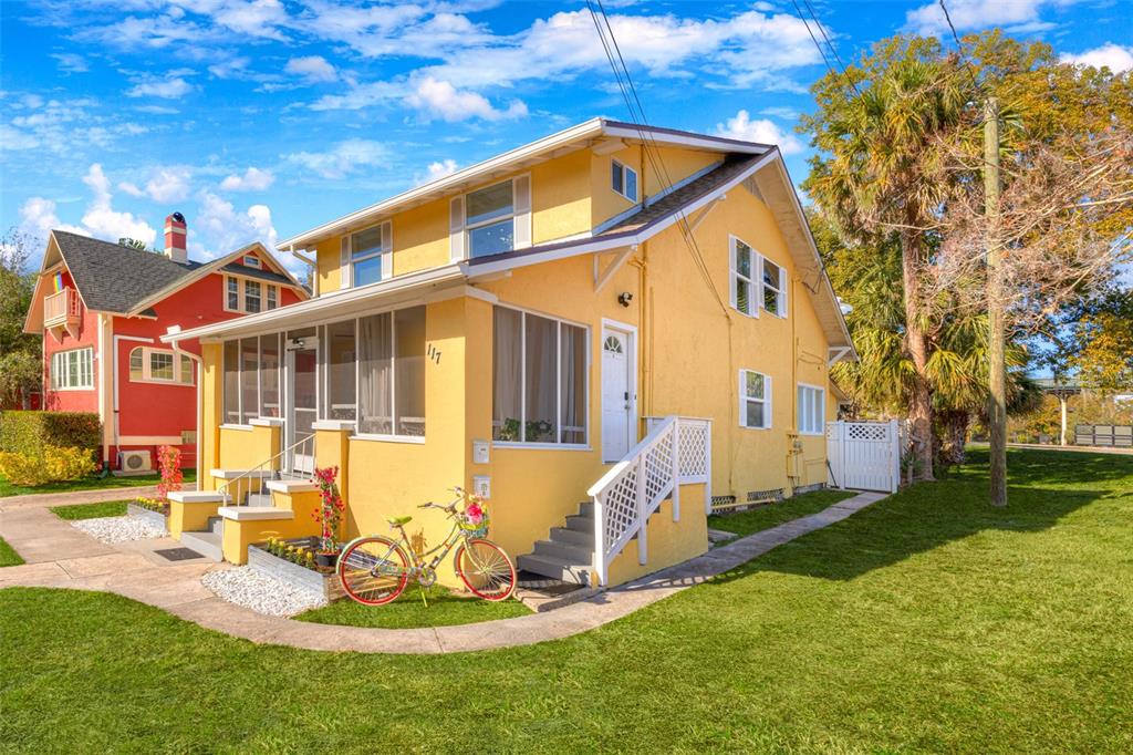 A yellow two-story house with a screened-in porch and a bicycle parked in the yard — 117 E EUCLID AVENUE, DELAND, FL