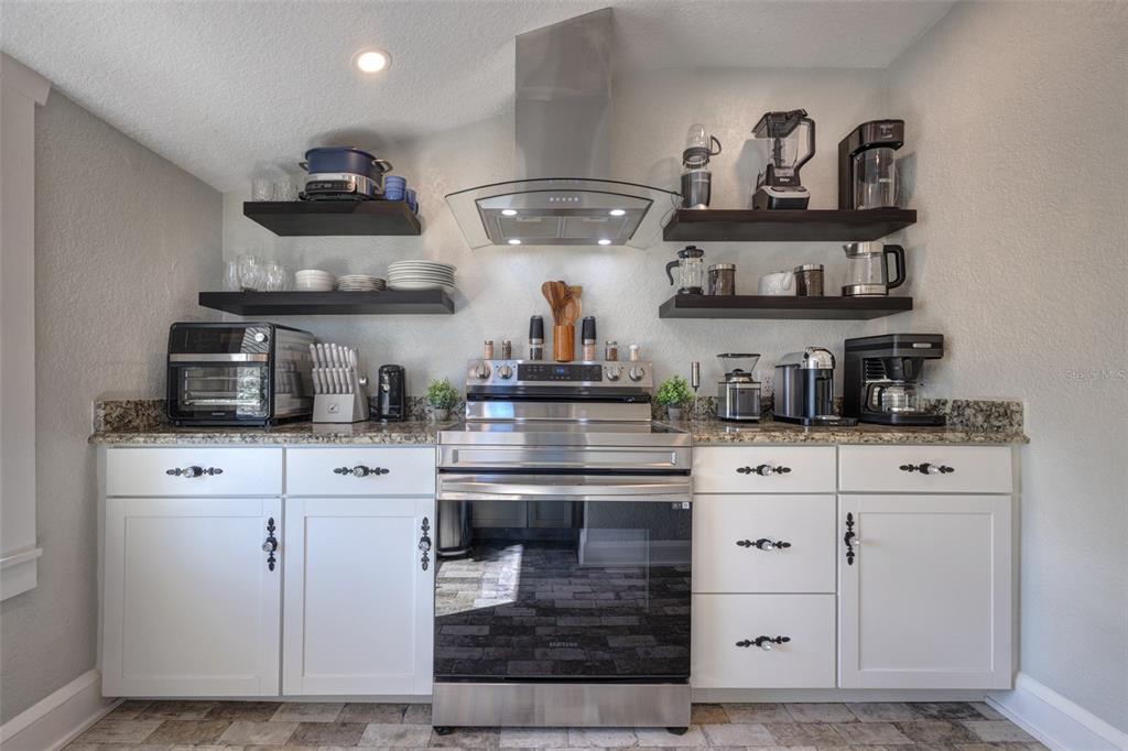 A kitchen features white cabinets, stainless steel appliances, open shelving, and granite countertops — 117 E EUCLID AVENUE, DELAND, FL