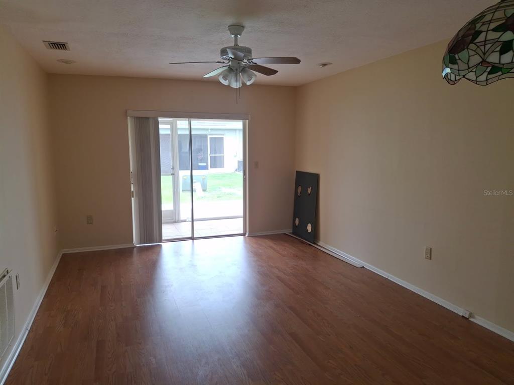 An empty living room features wood-look flooring, a ceiling fan, and sliding glass patio doors — 2931 STILLWELL COURT, NEW PORT RICHEY, FL