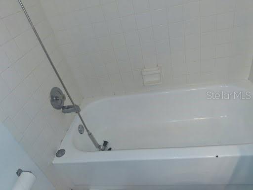 A white bathtub with a handheld shower head is set against a tiled wall — 2931 STILLWELL COURT, NEW PORT RICHEY, FL