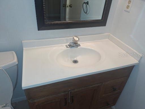 A bathroom vanity with a white countertop, single sink, and wooden cabinet below a mirror — 2931 STILLWELL COURT, NEW PORT RICHEY, FL