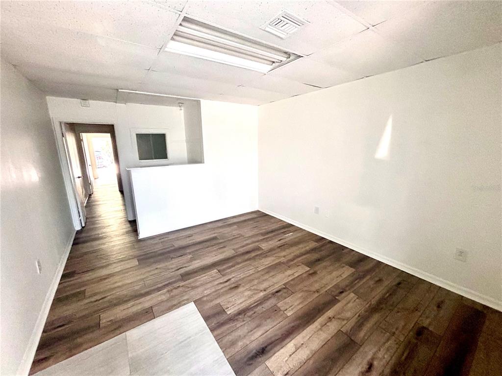 An empty room with wood-look flooring, white walls, and a drop ceiling with fluorescent lighting — 2201 S FRENCH AVENUE, SANFORD, FL