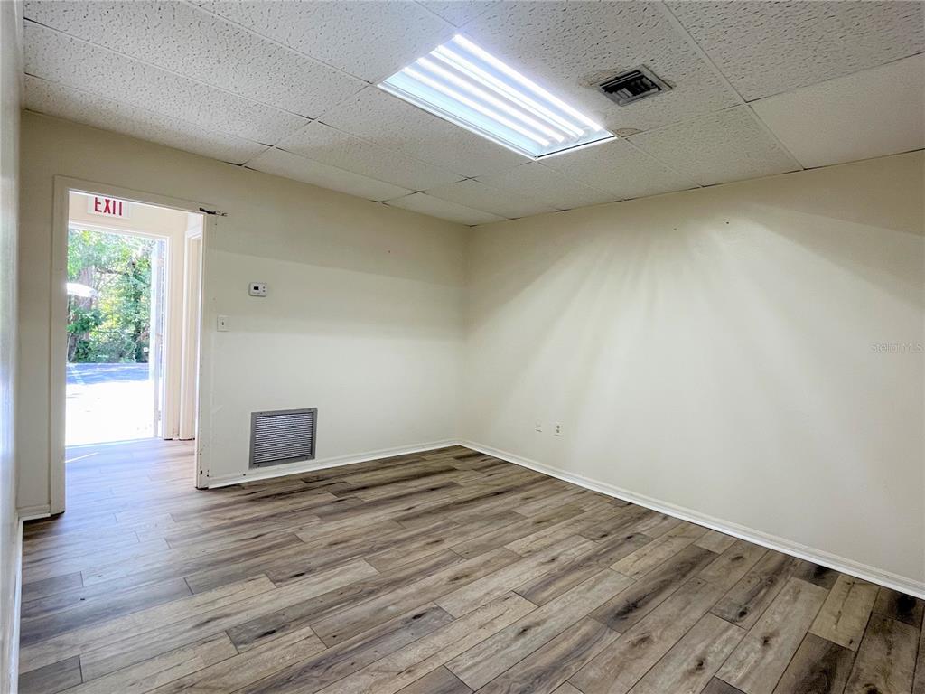 An empty room features wood-look flooring, a drop ceiling with a light fixture, and an exit — 2201 S FRENCH AVENUE, SANFORD, FL