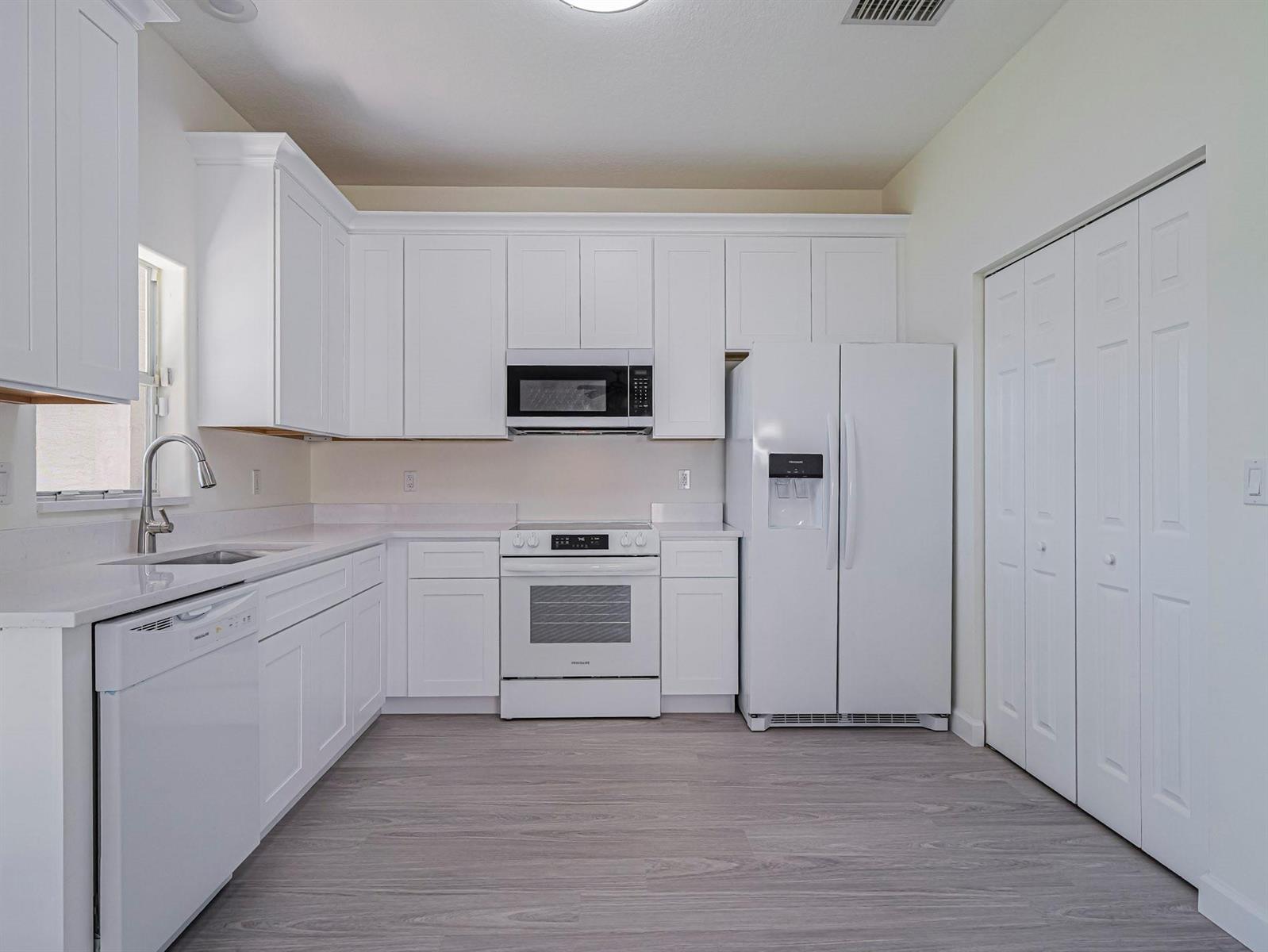 A kitchen with white cabinets, white appliances, light countertops, and gray wood-look flooring — 1834 77th Drive # 1834, Vero Beach FL 32966, VERO BEACH, FL