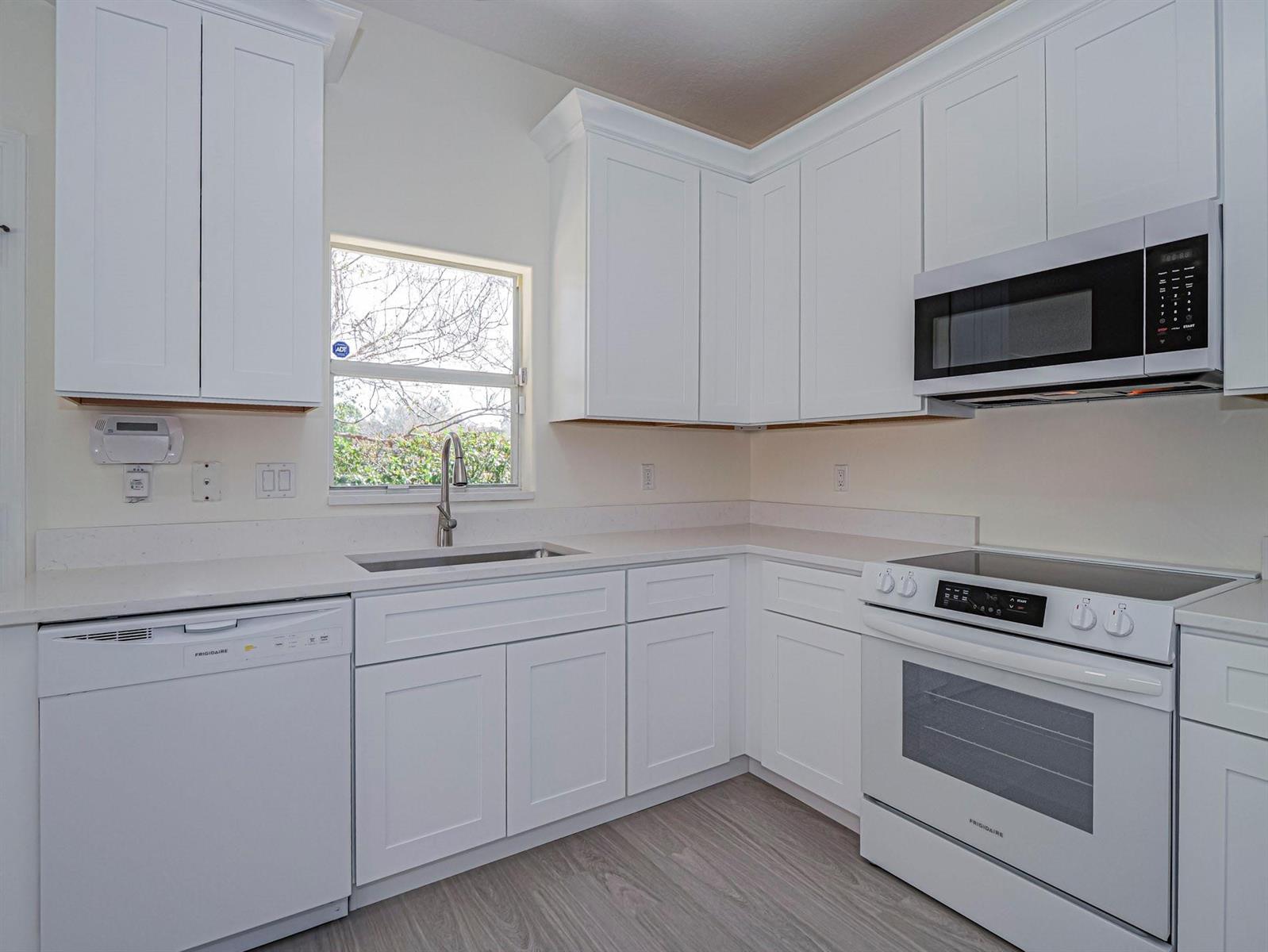 A bright kitchen features white cabinets, white appliances, a stainless steel sink, and light flooring — 1834 77th Drive # 1834, Vero Beach FL 32966, VERO BEACH, FL